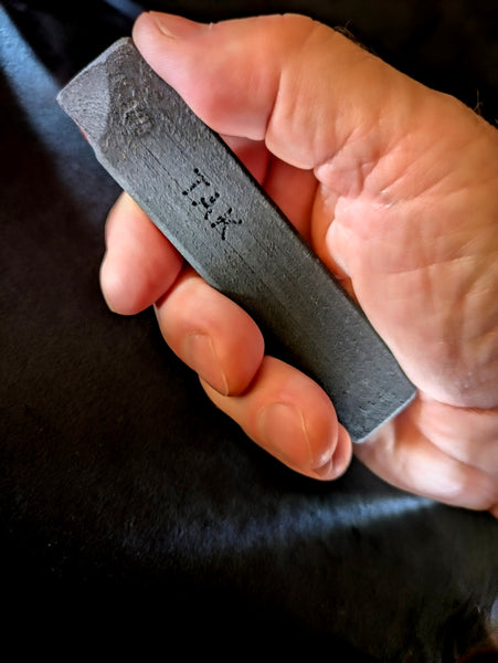 A close-up of a hand holding a dark gray training pop knife aka box cutter  engraved with the brand name 'TAK'.